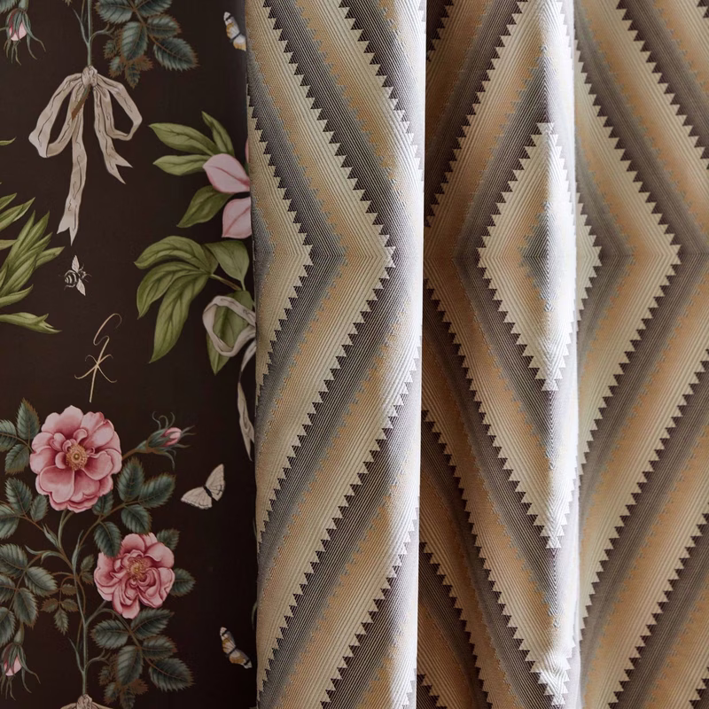 Fabric sample of Dazzle next to a dark floral wallpaper panel, with the cloth shown as hanging draped lengths of upholstery fabric.