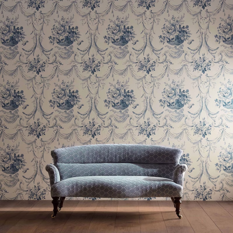 A patterned wallpapered room with a low sofa upholstered in the Faraday Velvet fabric in a blue-grey geometric design.