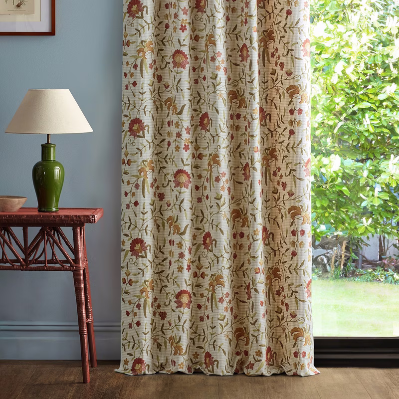 A room with floral patterned fabric hanging as curtains beside a window, with a lamp and side table nearby.