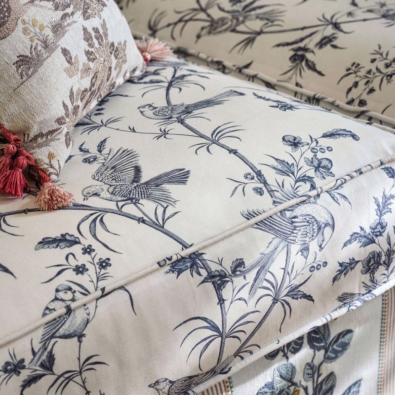 Close-up of a sofa upholstered in bird-and-branch toile fabric, with a matching patterned cushion and tasselled trim visible.
