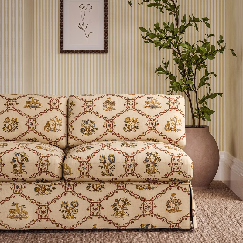 Living room with a sofa upholstered in patterned fabric, shown against striped wallpaper with a framed print and potted tree.
