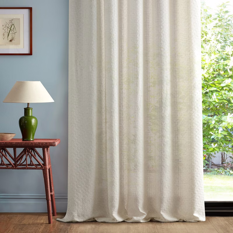 Light room interior with sheer fabric made up as curtains, hanging floor-length beside a window.