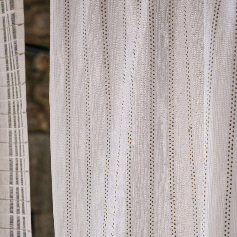 Light sheer curtains with vertical dotted stripes hang in front of a window, with another sheer panel visible at the left edge.