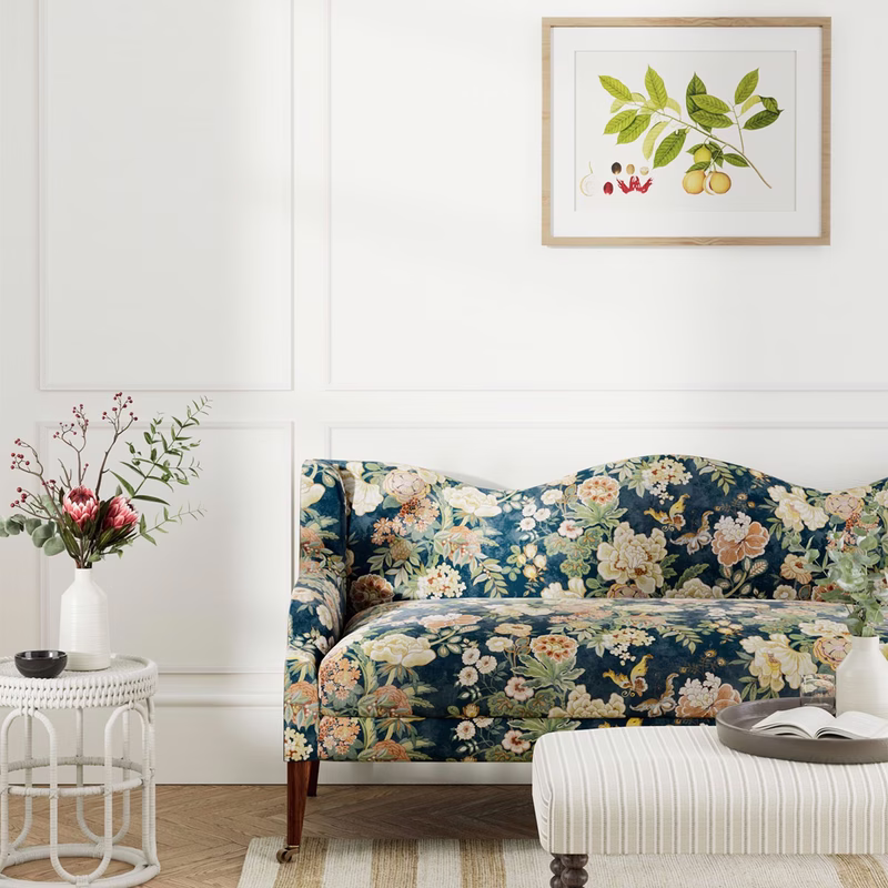 A room with a floral upholstered sofa, an ottoman and side table, showing the fabric made up as upholstery.