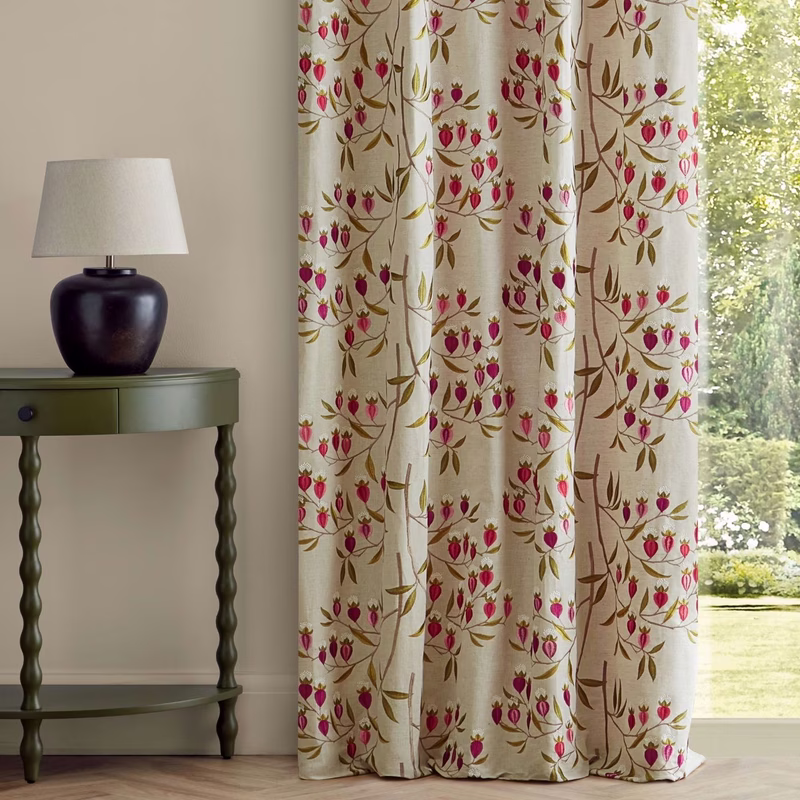 A room with a table lamp beside patterned curtains in cream with pink and brown floral motifs.
