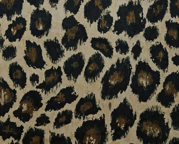 Warm beige fabric with irregular black and brown ocelot spots and textured brush-like edges