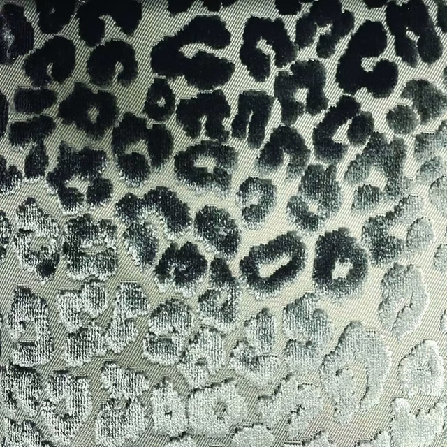 Pale sage woven fabric with irregular black cheetah spots and tactile diagonal texture