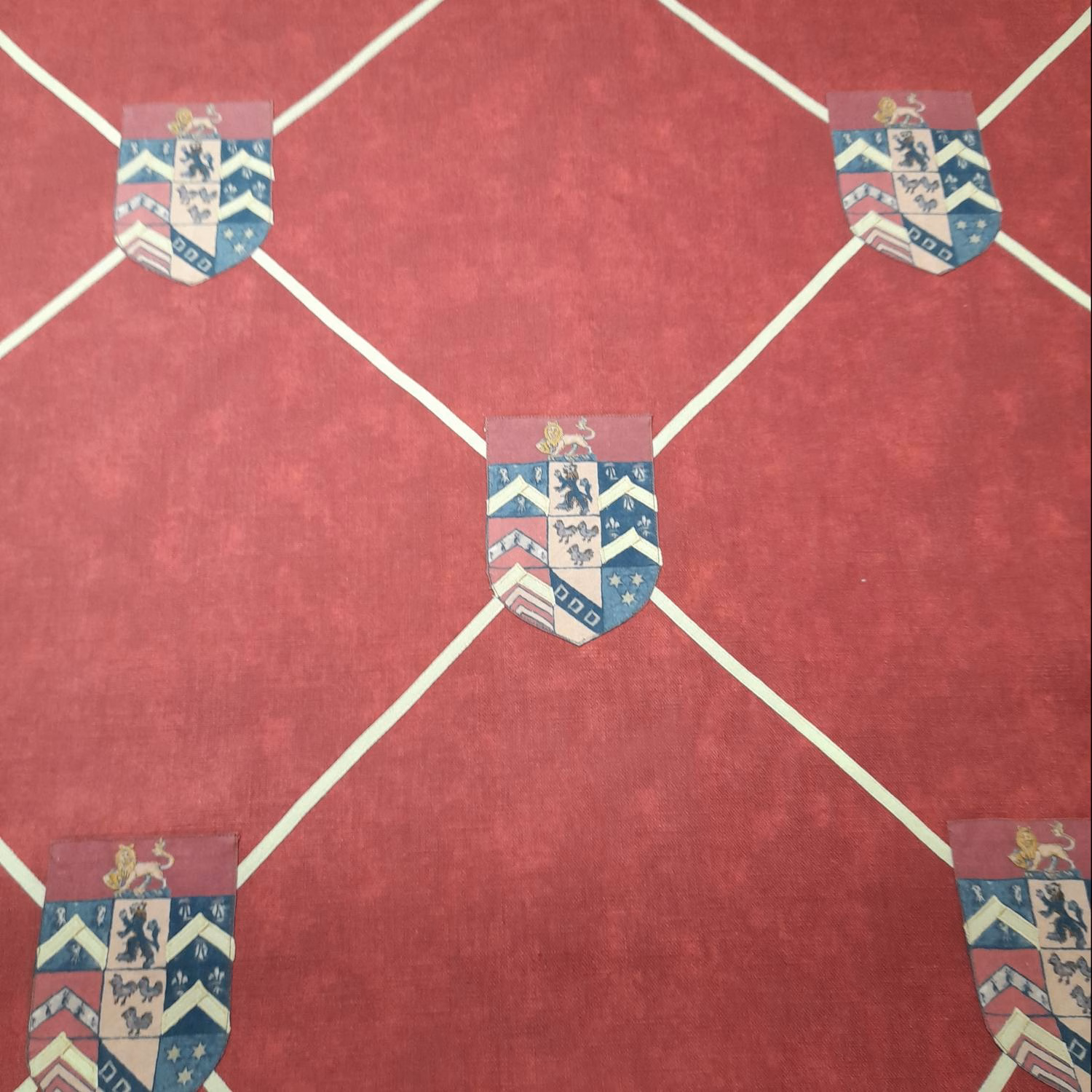Muted berry-red fabric with cream diamond lines and repeated heraldic shield emblems