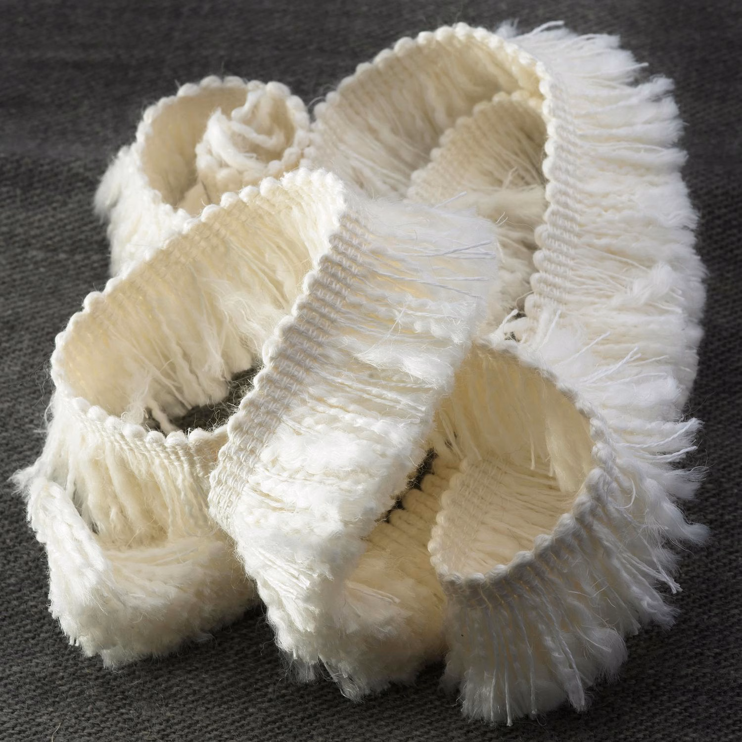 Warm ivory ribbed fringe textile coiled into layered loops on dark charcoal fabric