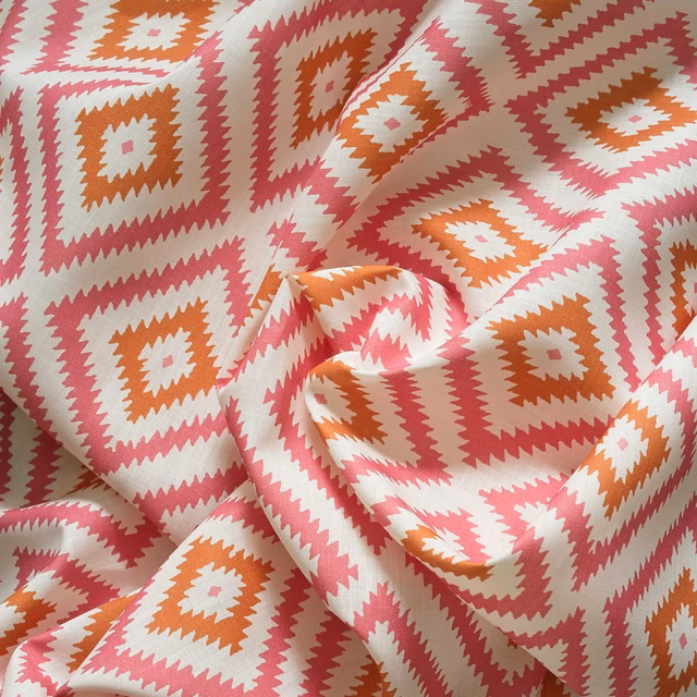 Coral pink and terracotta geometric diamond pattern on a cream outdoor fabric