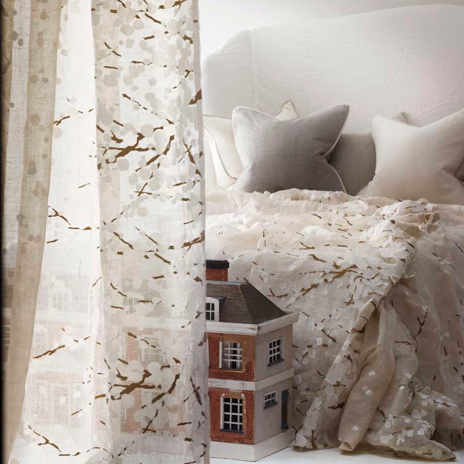 Warm ivory sheer fabric with sepia branch marks and pale leaves beside a layered bed
