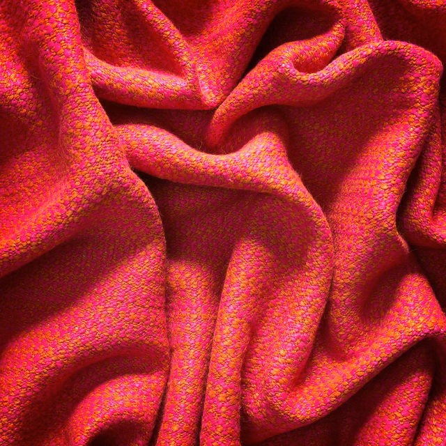 Draped magenta-pink woven fabric with orange flecks and a pronounced nubby texture
