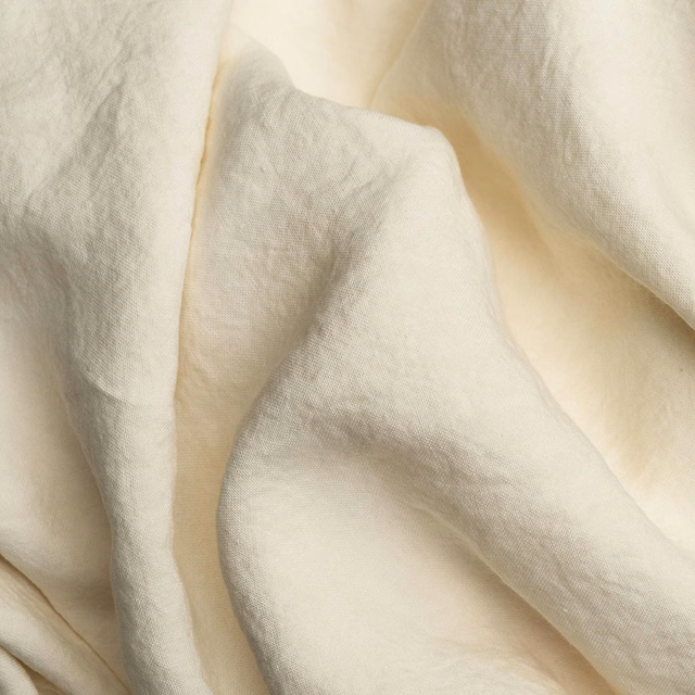 Warm ivory plain weave fabric draped in soft folds with a subtle natural texture