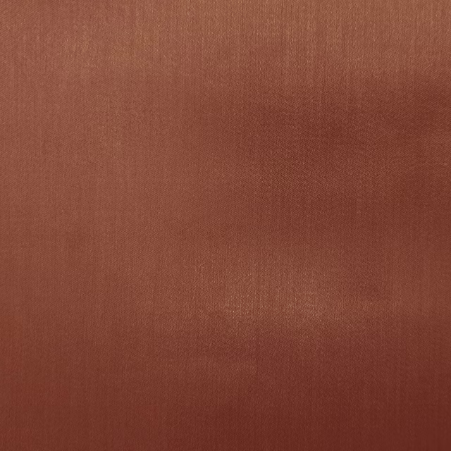 Close-up of a smooth plain fabric in warm rust terracotta with a soft sheen