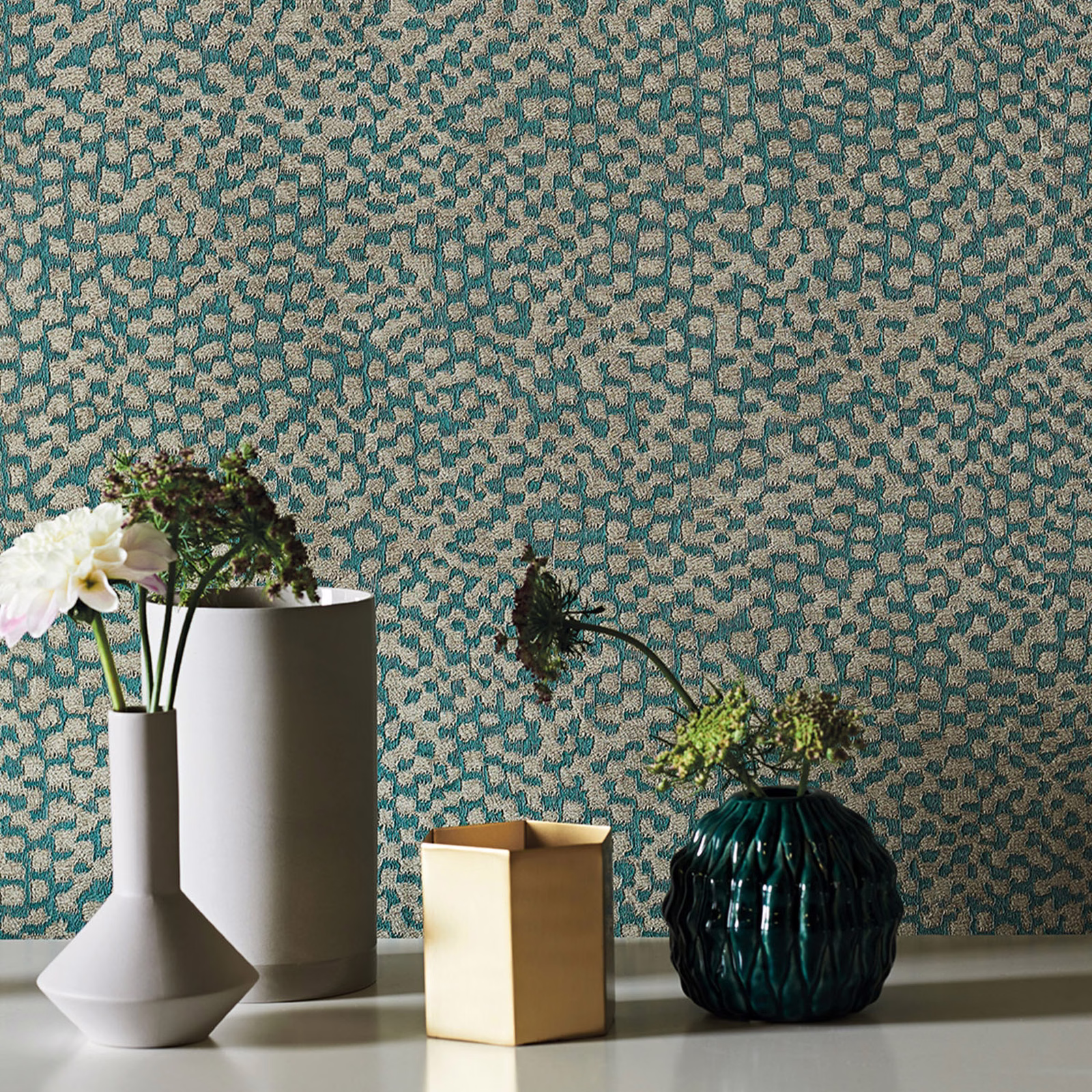 Muted teal wallpaper with small irregular beige geometric marks behind sculptural vases