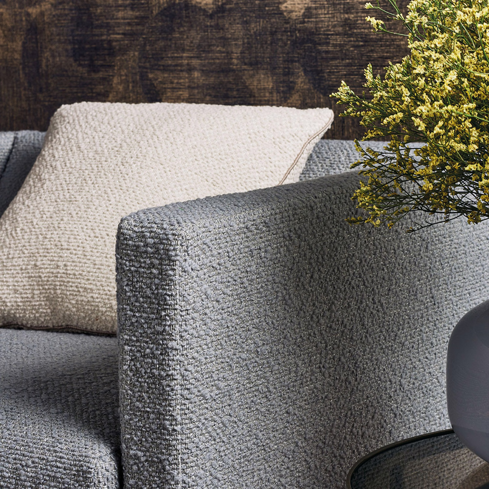 Cool charcoal-grey nubby upholstery on a rounded arm beside cream cushions