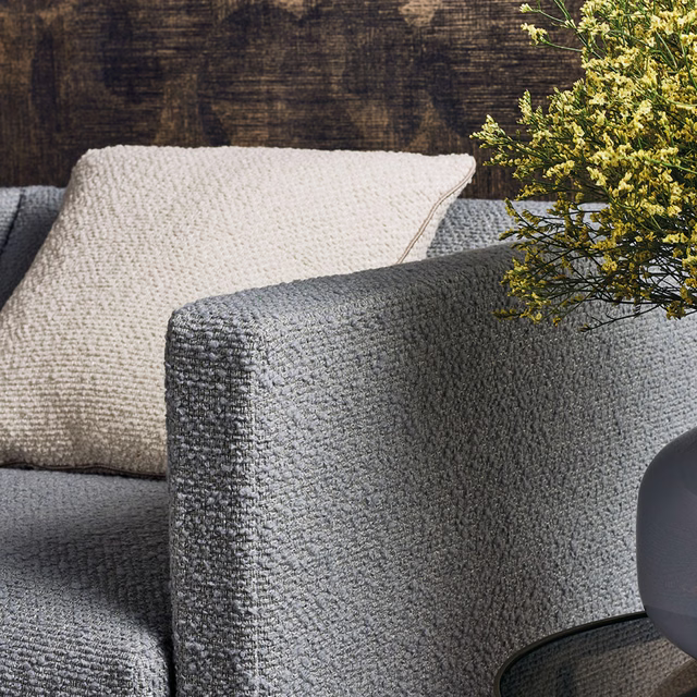 Cool charcoal-grey nubby upholstery on a rounded arm beside cream cushions