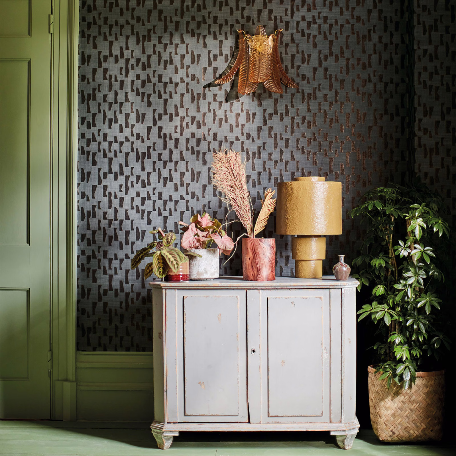 Charcoal wallpaper with repeating copper geometric marks beside green cabinetry