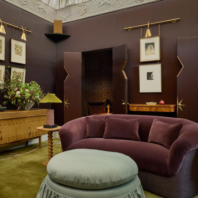 Deep cumin-brown wallcovering creating a dark, softly textured backdrop behind a curved burgundy sofa