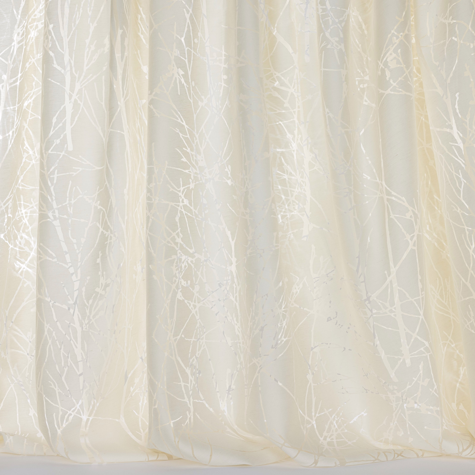 Cream sheer curtain fabric with pale tree-branch pattern and soft vertical folds