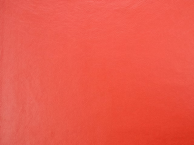 Vivid coral-red faux leather with a fine pebbled grain and subtle sheen