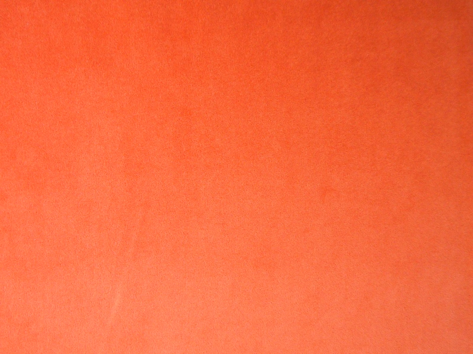 Close-up of warm coral-orange velvet with a softly shaded, textured pile surface