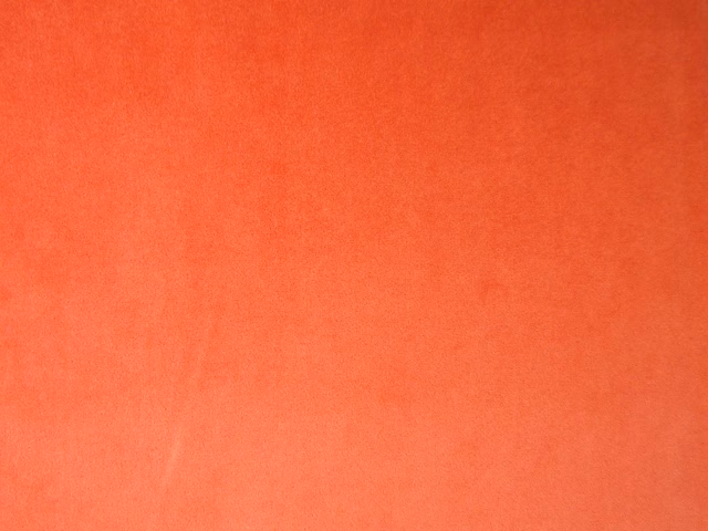 Close-up of warm coral-orange velvet with a softly shaded, textured pile surface