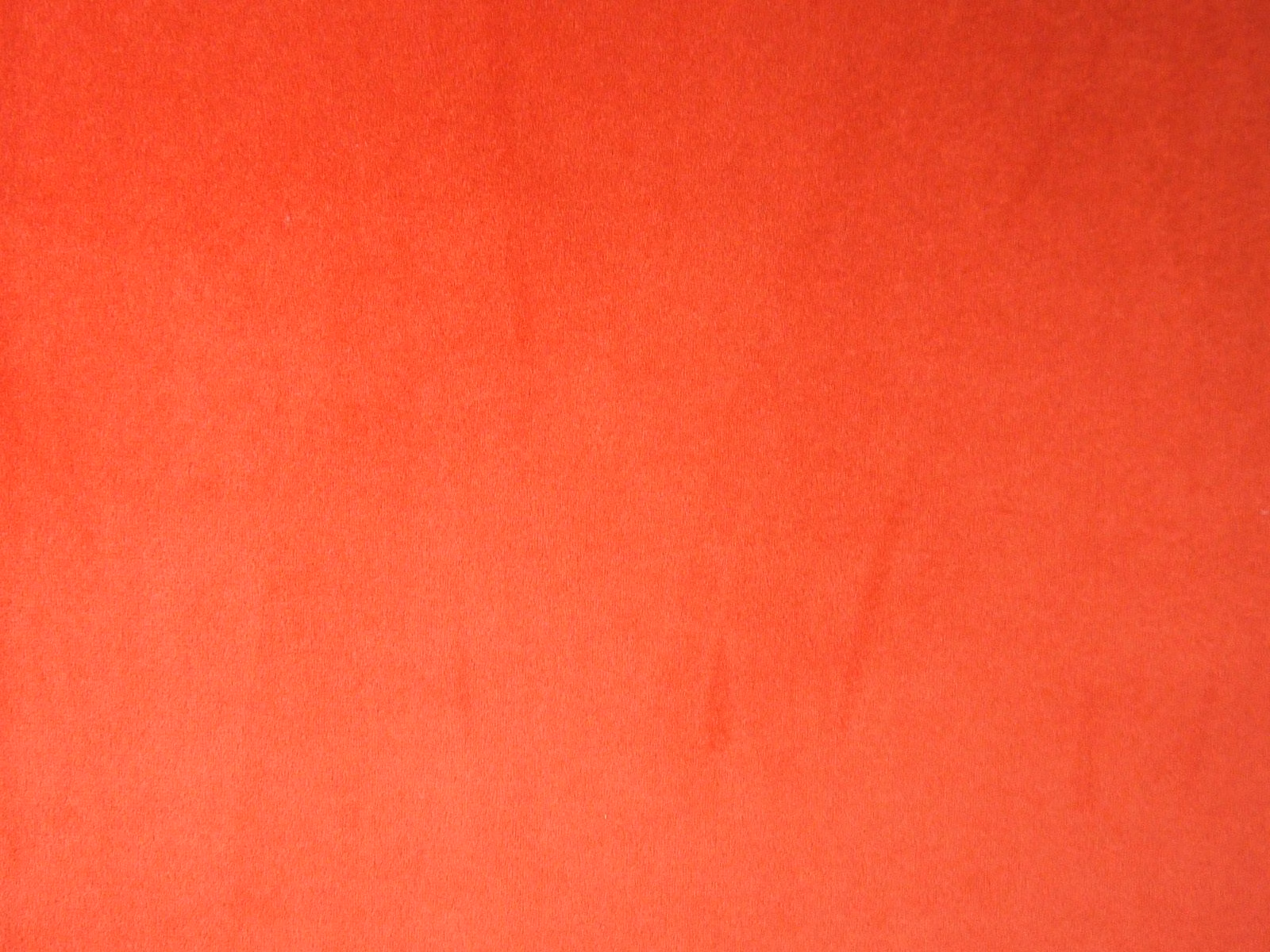 Close-up of plain coral-red velvet with softly shifting nap and fine pile