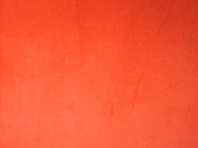 Close-up of plain coral-red velvet with softly shifting nap and fine pile