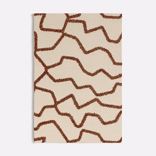 Warm cream textile with raised rust-brown meandering lines and fine woven texture