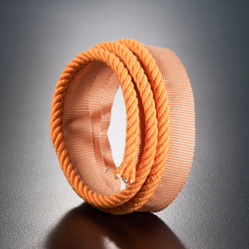 Warm coral-orange woven textile with raised twisted cord edging, shown rolled