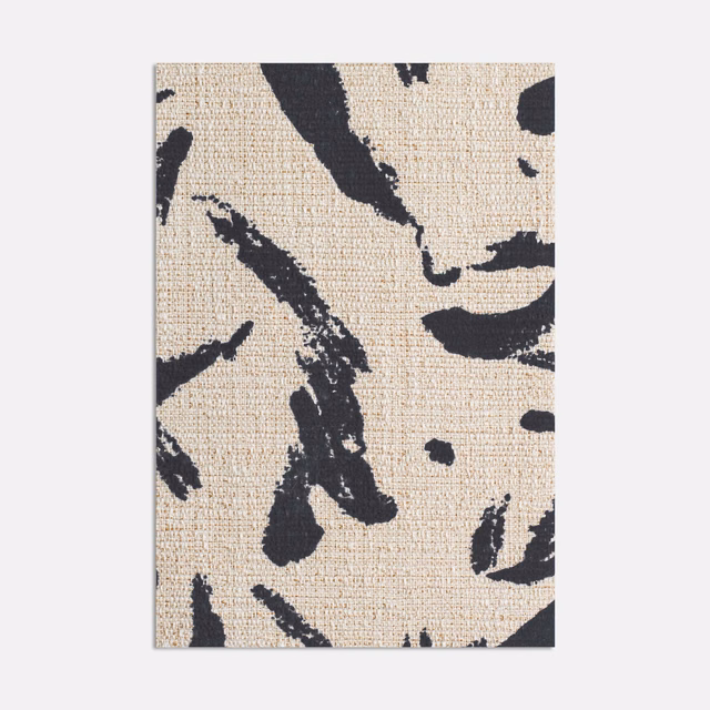 Warm beige woven fabric with bold black abstract brush strokes and scattered flecks