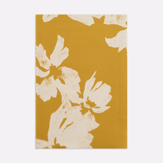 Warm ochre fabric with oversized ivory botanical blooms and subtle woven grain