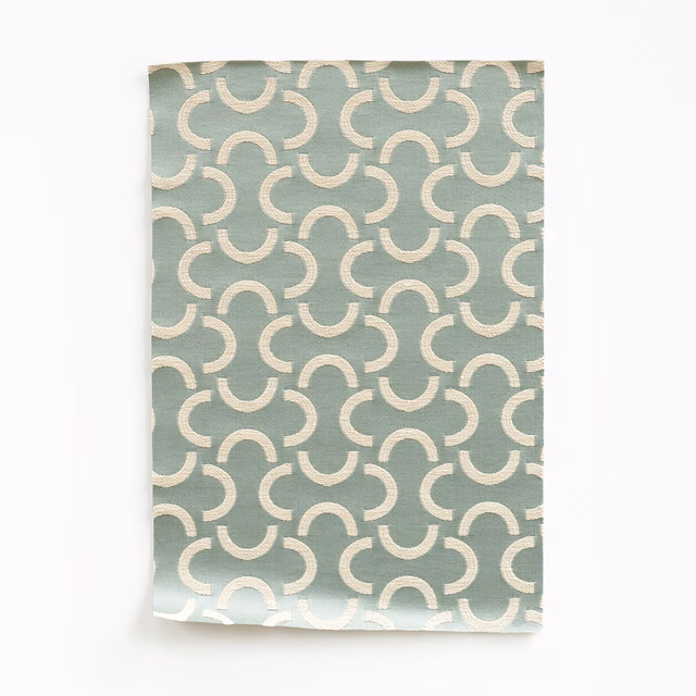 Muted sage-green satin swatch with repeating ivory curved motifs and subtle sheen