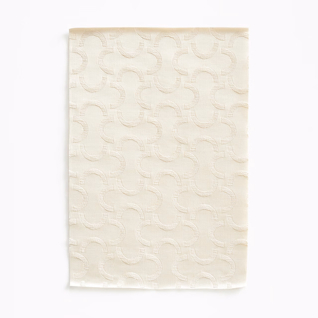 Warm ivory satin swatch with raised interlocking curved motifs and a gentle sheen