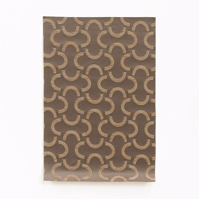 Warm taupe fabric with repeating beige-gold interlocking crescent motifs and a softly textured weave