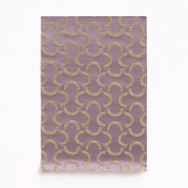 Mauve-lilac satin swatch with repeating brushed-gold interlocking crescent motifs