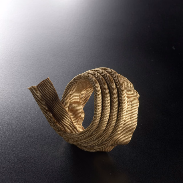 Coiled hazelnut-brown ribbed cord with antique-gold highlights on a dark surface