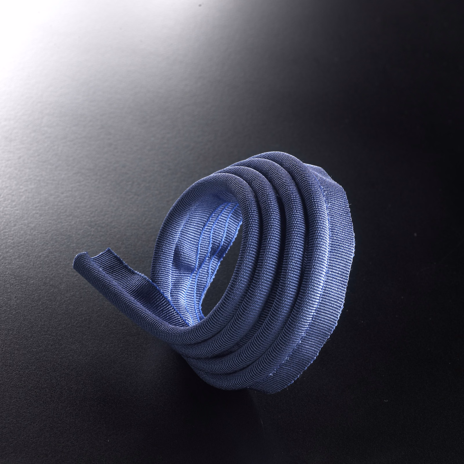 Cool porcelain-blue ribbed lipcord coiled into a compact loop against black