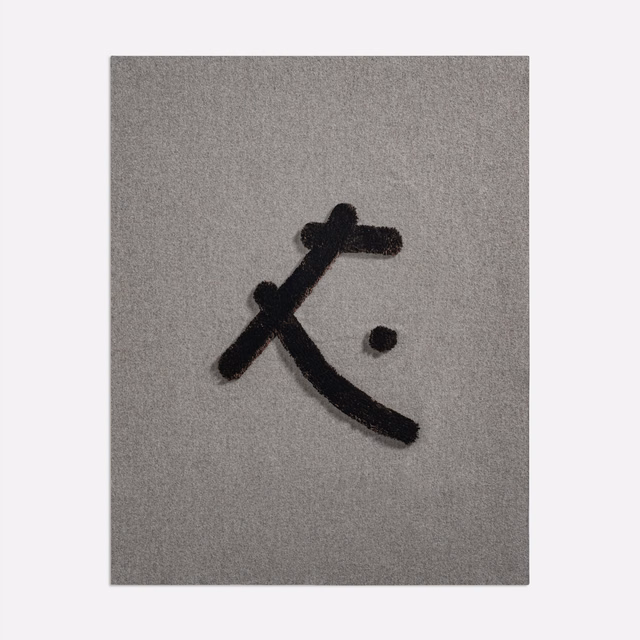 Taupe-grey woven fabric with a raised black abstract mark and separate dot