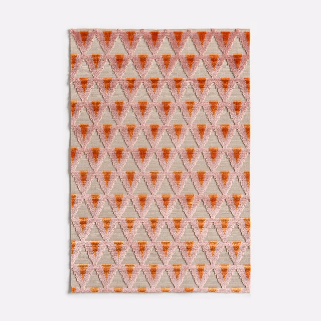 Warm coral and blush velvet swatch with repeating small hourglass motifs and woven texture