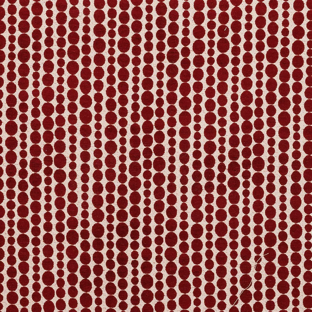 Red polka-dot patterned fabric swatch on a pale ground, with woven texture
