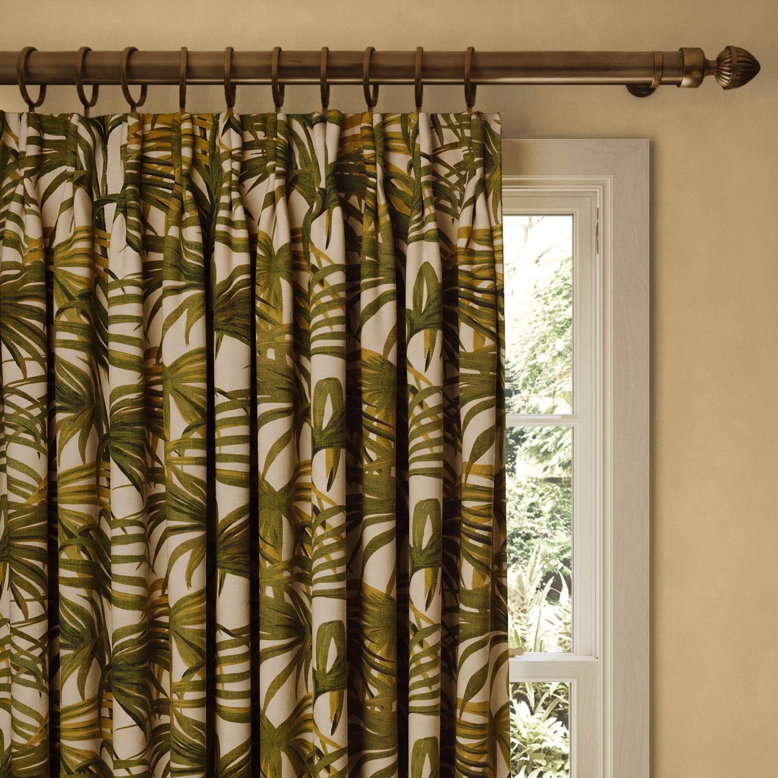 Pleated off-white curtain with olive green tropical palm leaves beside a bright window