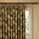 Pleated off-white curtain with olive green tropical palm leaves beside a bright window