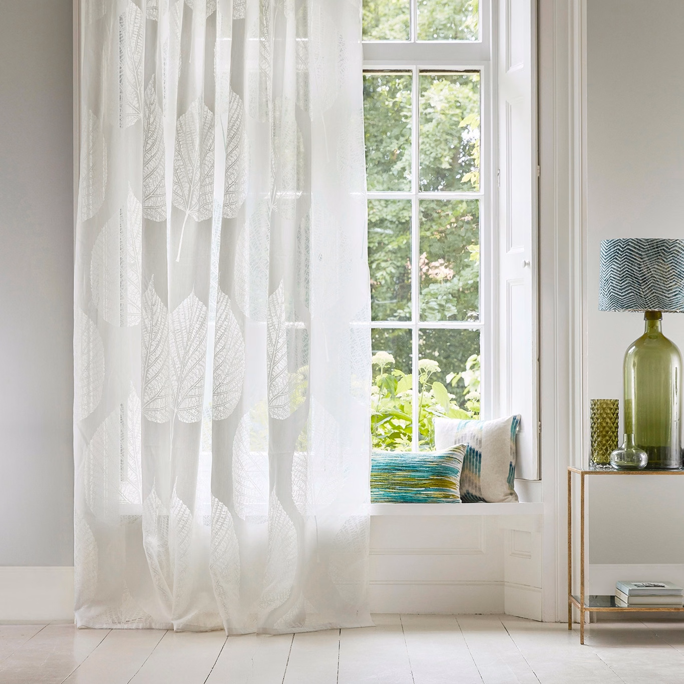 Chalk-white sheer curtain with translucent elongated leaf motifs beside a bright window