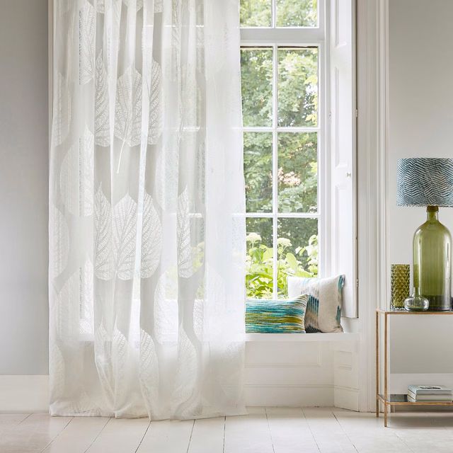 Chalk-white sheer curtain with translucent elongated leaf motifs beside a bright window