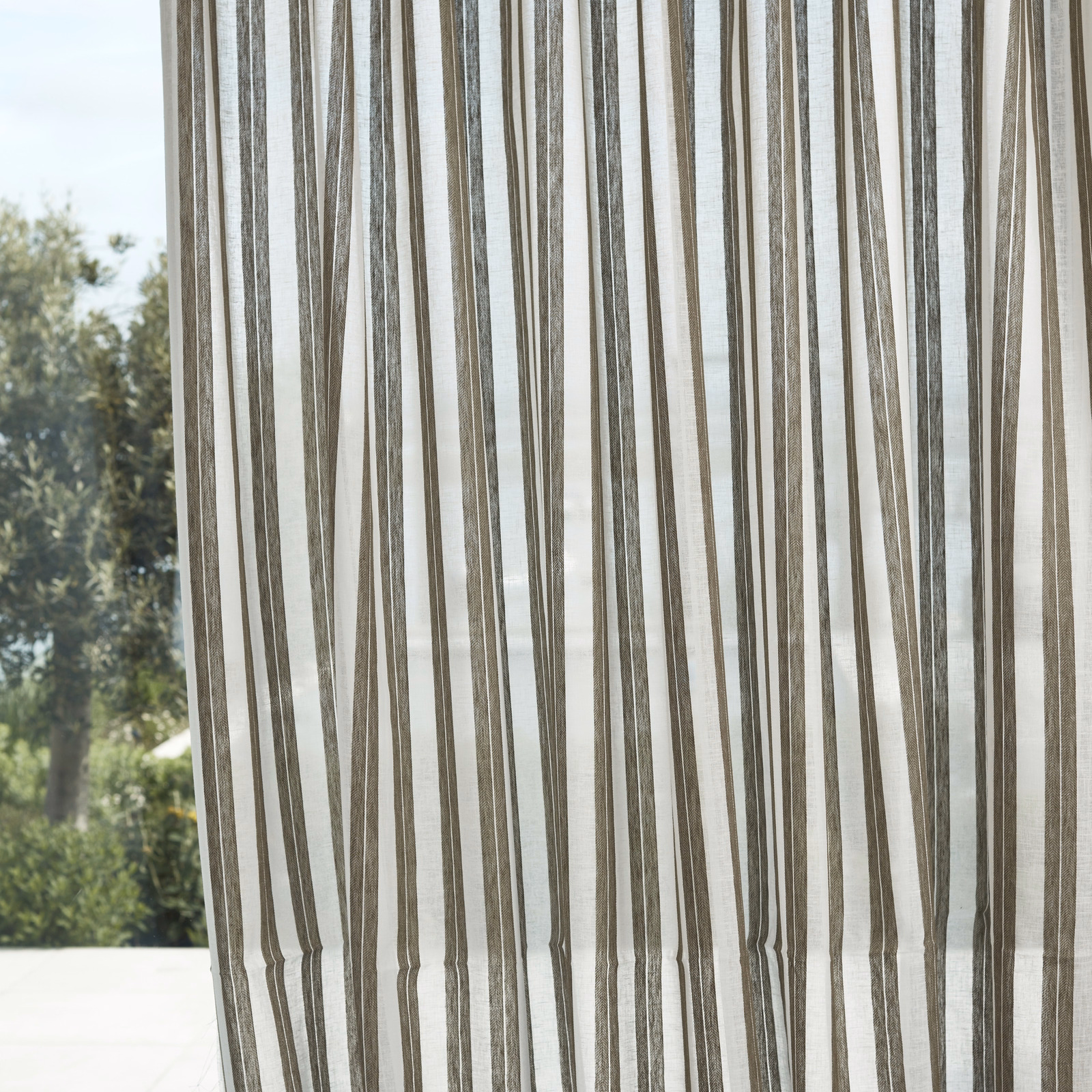 Translucent olive sheer with irregular vertical stripes glowing against a pale daylight background