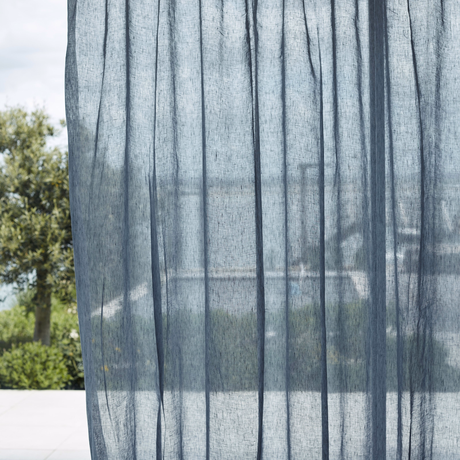 Blue-grey sheer curtain with fine dark vertical lines and visible garden beyond