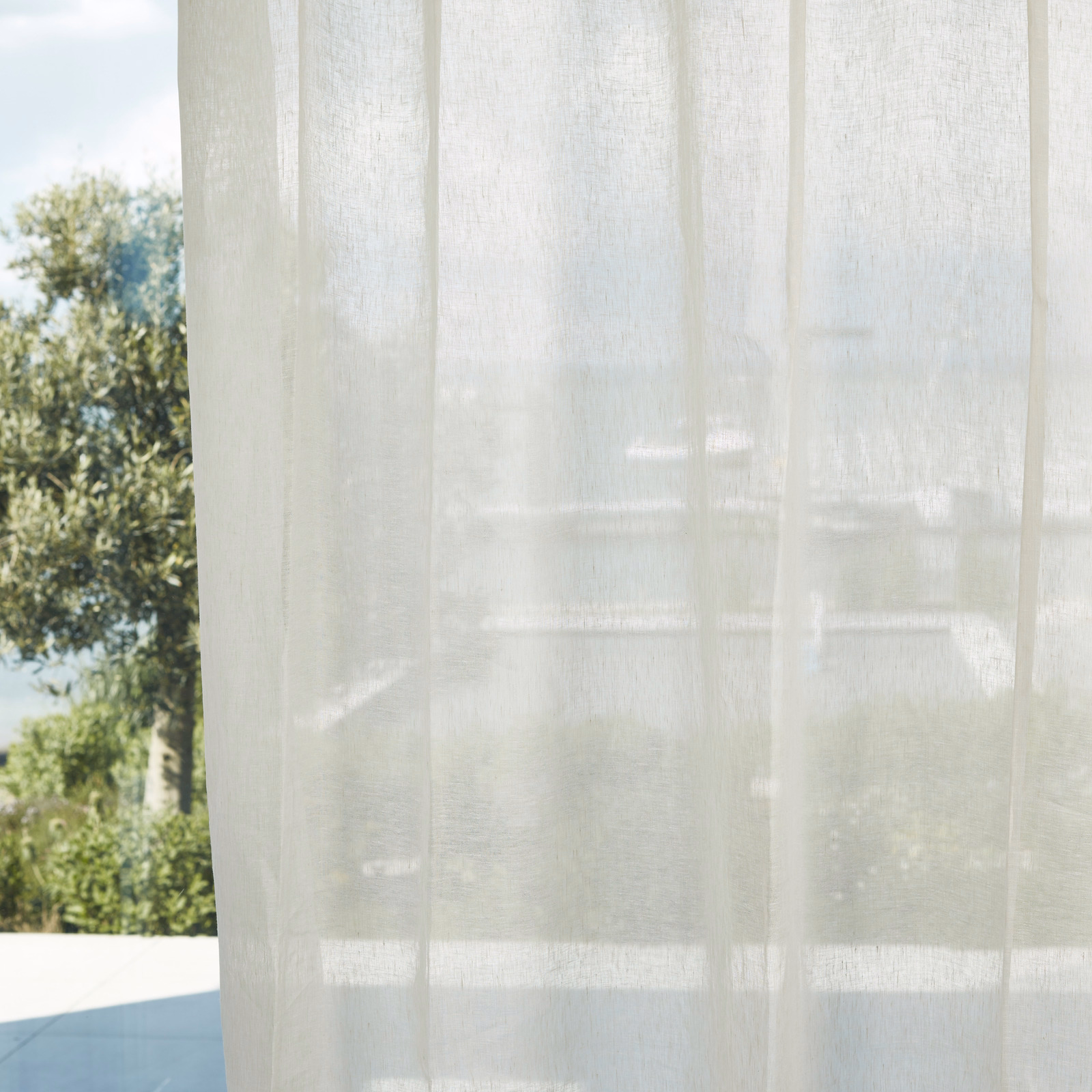 Translucent chalk-white sheer with fine vertical weave filtering a sunlit garden view