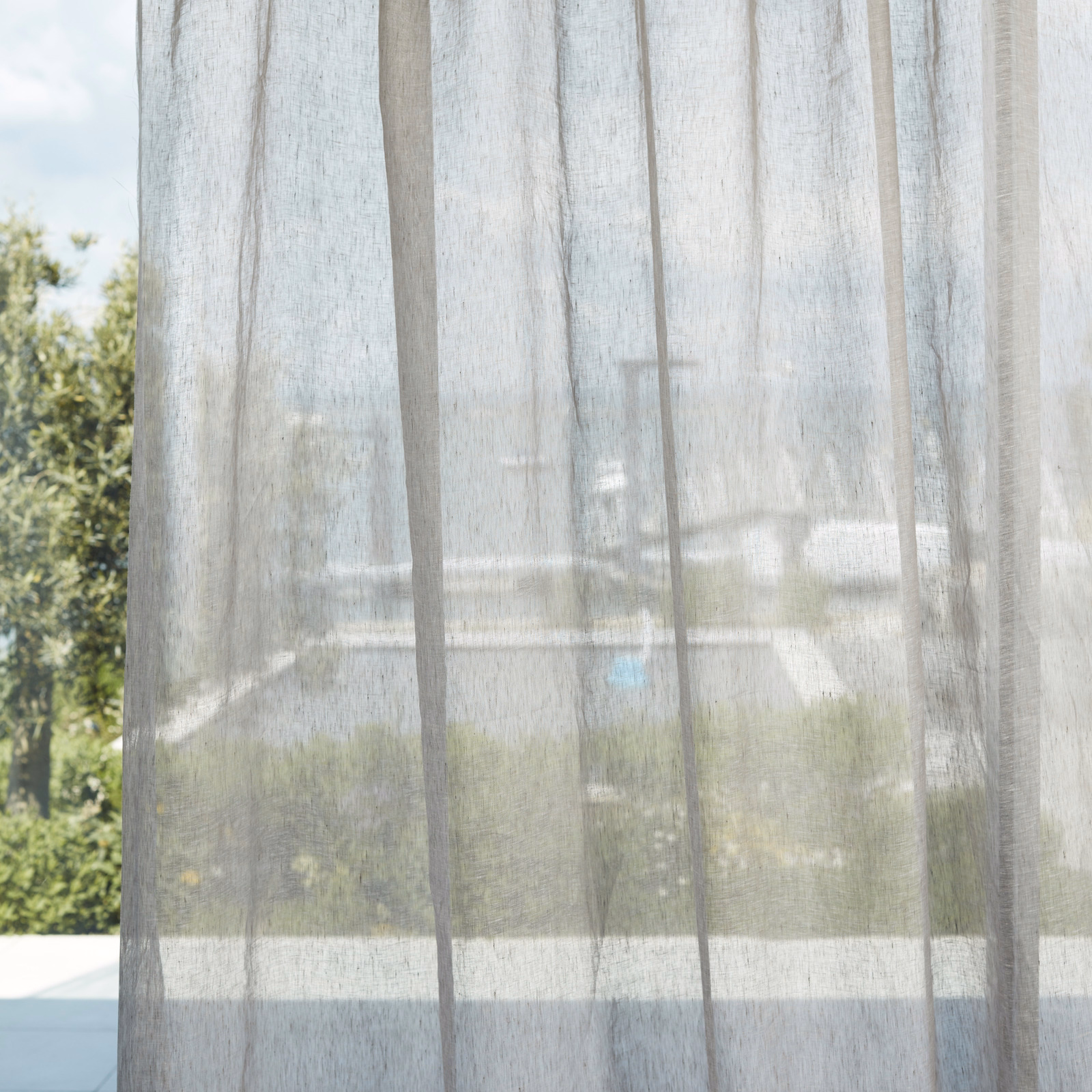 Pale greige sheer with fine vertical weave filtering a sunlit garden view